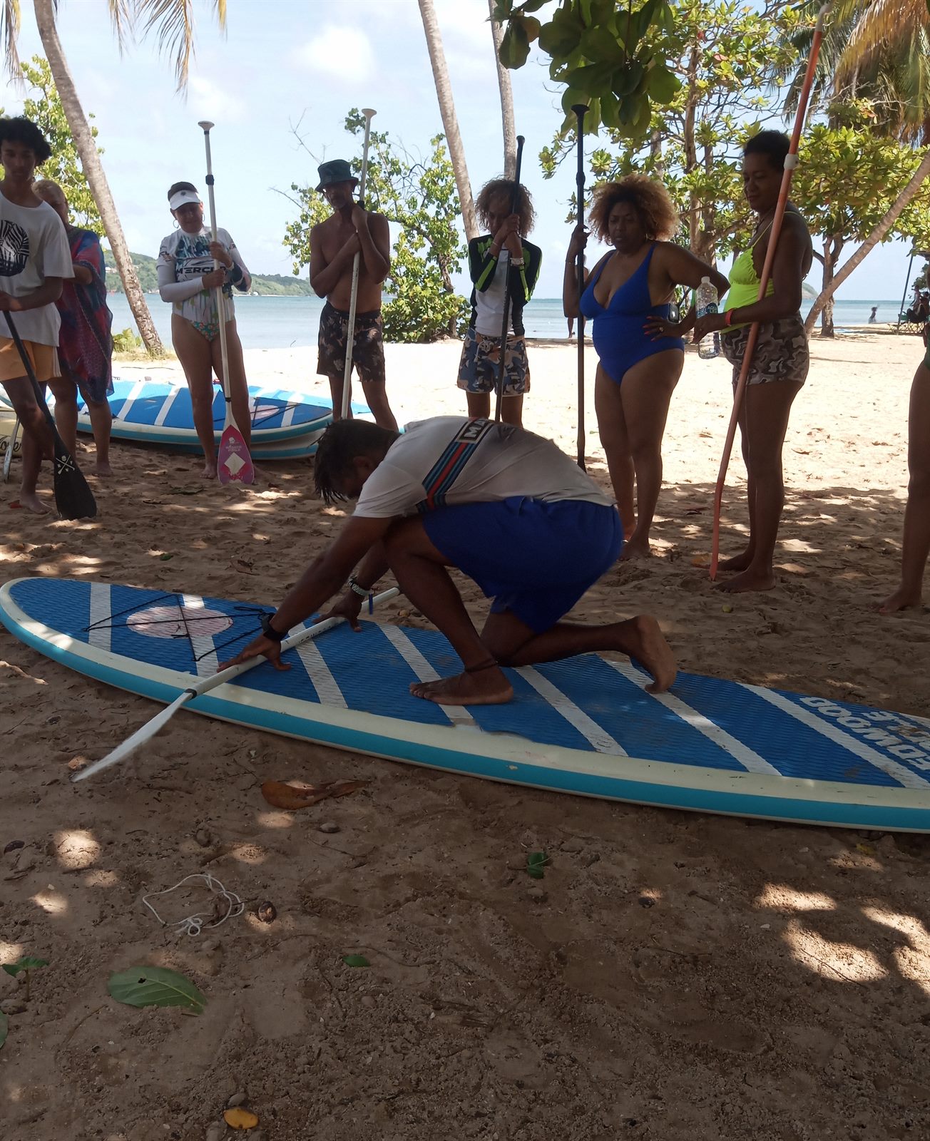 L'éducateur montre la position à genoux sur la planche, sur la plage