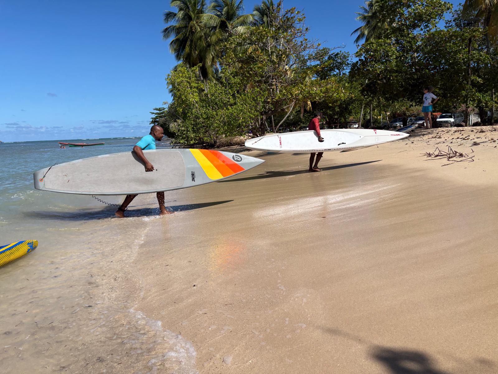 Deux pratiquants portent leurs planches vers l'eau