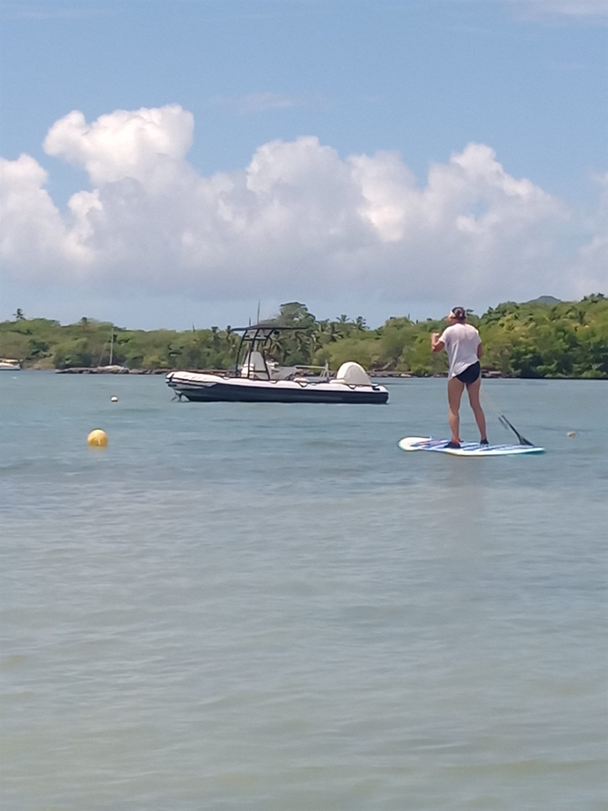 Une pratiquante debout sur sa planche, près d'un bateau au mouillage